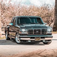 a black pickup truck parked on the side of a road next to trees and bushes