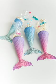 three little mermaid tail shaped popcorn cones on a white table with sprinkles