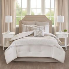 a white bed in a bedroom next to a window with curtains and two nightstands