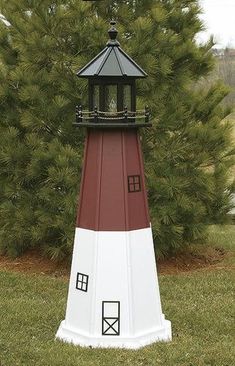 a red and white light house sitting on top of a lush green field next to a pine tree