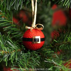 a red golf ball ornament hanging from a christmas tree decorated with gold ribbon