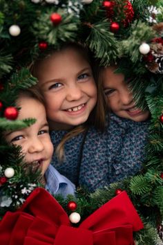 three children are peeking out from behind a christmas wreath