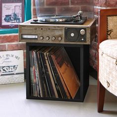 a record player sitting on top of a wooden table next to a chair and wall