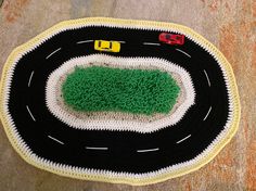 a crocheted rug with cars driving on the road and grass in the middle