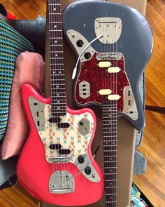 two guitars are sitting next to each other on top of a suitcase, one is red and the other is blue