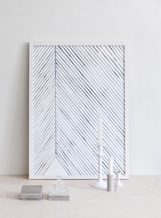 two candles are sitting on a table next to a white frame with diagonal lines in it