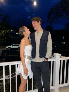 a man standing next to a woman on top of a white balcony near a fence