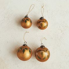 four ornaments hanging from strings on a white wall, each with green leaves painted on them