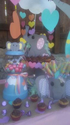 there are many cupcakes on the table with elephants and hearts hanging from them