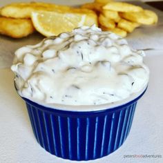 a blue cup filled with white sauce next to some fried potatoes and lemon wedges