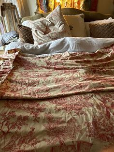 an unmade bed with red and white sheets on it in front of a window