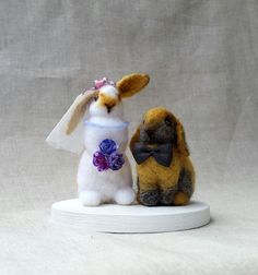 two stuffed animals dressed up as rabbits on a white base, one is wearing a dress and the other has a bow tie