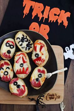 a black plate topped with mini pizzas on top of a wooden cutting board next to a halloween t - shirt