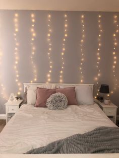 a white bed topped with lots of lights next to a night stand filled with pillows