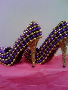 purple and gold high heeled shoes with pearls on the toes are sitting on a pink surface