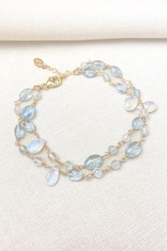 This bracelet showcases delicate moss aquamarine gemstones paired with radiant rainbow moonstones, creating a lovely, feminine style. The artisan meticulously hand-wire-wraps each gemstone bead, creating a beautiful, double-layered chain. The lobster claw clasp and extender chain allow for an adjustable fit. Bracelet length: 7 inches plus 1-inch extender chain Materials: aquamarine, rainbow moonstone, gold fll Elegant Aquamarine Beaded Bracelets With Natural Stones, Dainty Blue Moonstone Jewelry, Elegant Moonstone Gemstone Beaded Bracelets, Elegant Aquamarine Bracelets With Natural Stones, Elegant Hand Wrapped Moonstone Jewelry, Elegant Hand-wrapped Moonstone Jewelry, Moss Aquamarine, Layered Chain, The Lobster