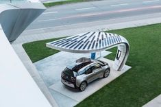 an electric car is parked under a metal structure on the grass near a street corner