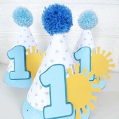 three party hats with blue pom - poms on them, one for the first birthday