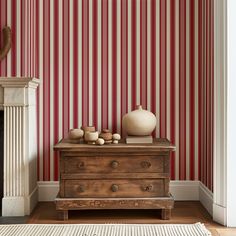 a room with red and white striped wallpaper, a chest of drawers and vases