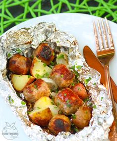 a plate with potatoes and meat wrapped in foil next to a fork on a green tablecloth