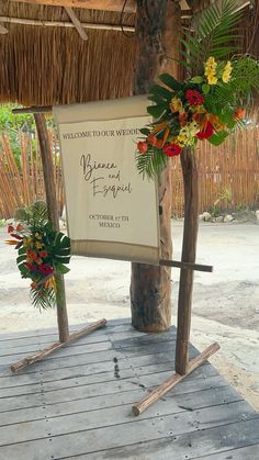 a welcome sign with tropical flowers and greenery in front of a tiki hut