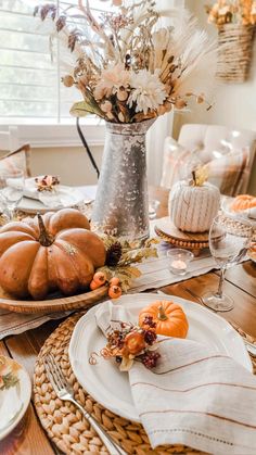 a table set for thanksgiving with pumpkins and flowers in a vase on the side