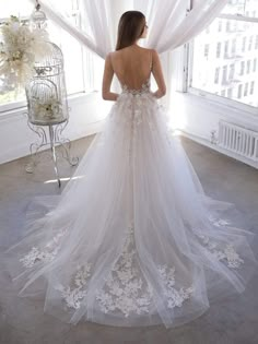 a woman standing in front of a window wearing a wedding dress with flowers on it