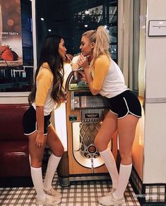 two women in short shorts and knee high boots standing next to each other, one is biting into another woman's mouth