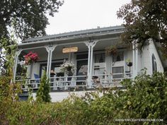 a white house sitting on top of a lush green hillside next to trees and bushes