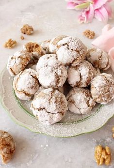 a plate full of powdered sugar cookies and walnuts on a table with pink flowers in the background