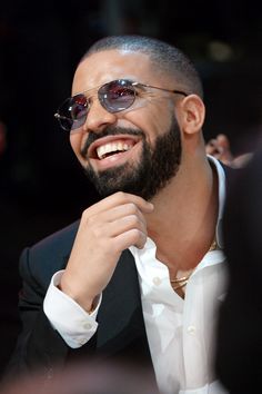 a man wearing sunglasses smiles while sitting in front of other people at a convention or event