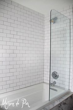 a bathtub with a glass shower door in a white tiled bathroom, next to a sink and toilet