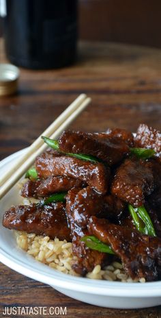 meat and rice on a white plate with chopsticks next to it, sitting on a wooden table