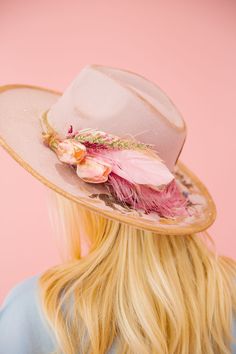 the back of a woman's head wearing a hat with feathers and flowers on it