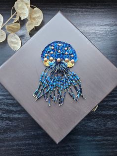 a blue brooch sitting on top of a wooden table next to a leafy plant