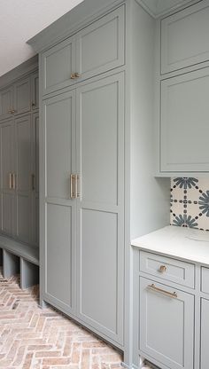 a kitchen with gray cabinets and white counter tops on brick flooring in front of an oven