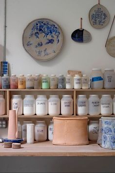 the shelves are filled with different types of jars and pottery on display in front of wall hangings