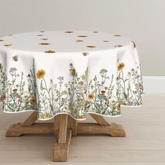 a white table cloth with yellow and red flowers on it sitting on a wooden stand