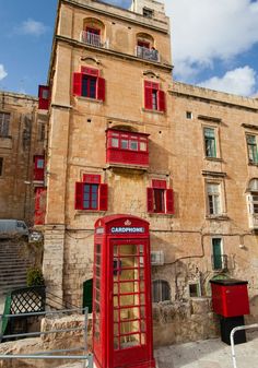 a red phone booth sitting in front of a tall brown building with red shutters