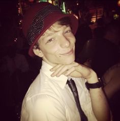 a young man wearing a red hat and tie posing for a photo with his hand on his chin