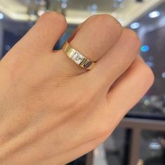 a person's hand wearing a gold ring with two diamonds on it, in front of a window