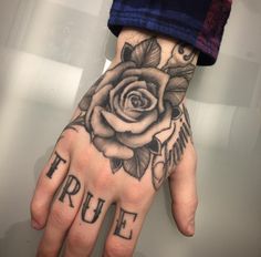 a person's hand with a rose tattoo on it and the word true written in black ink