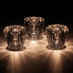 three glass candle holders sitting on top of a table next to each other in the dark