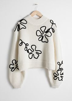 a white sweater with black and white flowers on the front is hanging from a hanger