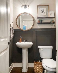 a white toilet sitting next to a sink in a bathroom under a round mirror on the wall