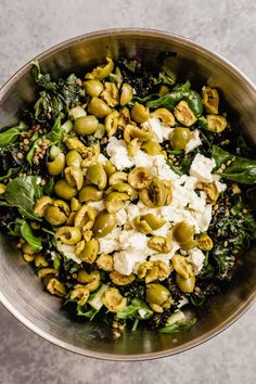 a metal bowl filled with green vegetables and feta cheese, on top of a table