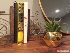 a wooden table topped with books and a gold vase filled with plants next to a mirror