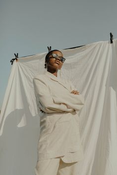 a man wearing sunglasses standing in front of a white sheet with his hands on his hips