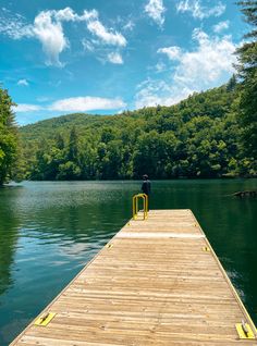 a person standing on a dock in the middle of a body of water surrounded by trees