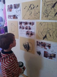 a young boy standing in front of a wall covered in drawings